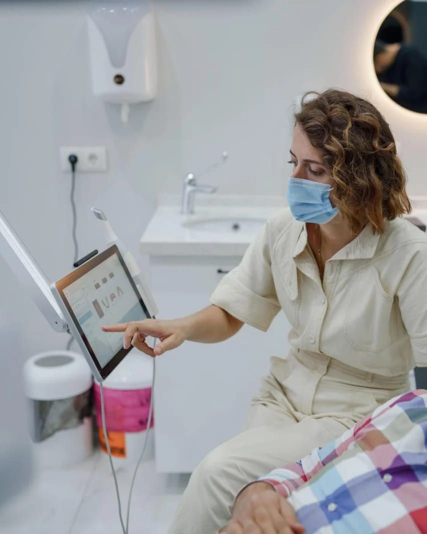 A dentist pointing at a digital smile design on a screen beside a patient